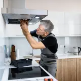 Ein Handwerker repariert eine Dunstabzugshaube, die nicht mehr angeht. Er schaut konzentriert hinein und arbeitet mit Werkzeug.