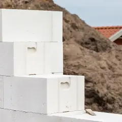 Baustelle: Stapel von Porenbetonsteinen warten darauf, verputzt zu werden. Im Hintergrund ein kleineres Gebäude.