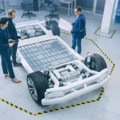 Ingenieure diskutieren über die e-auto batterie als pv speicher, die in einem modernen Labor auf einem Chassis montiert ist.