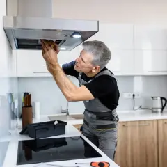 Ein Handwerker repariert eine Dunstabzugshaube, die nicht mehr angeht. Er schaut konzentriert hinein und arbeitet mit Werkzeug.