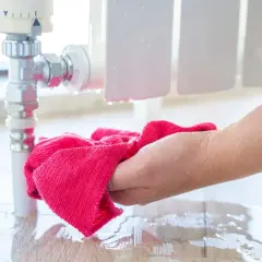 Hand wischt Wasser auf dem Boden auf, das aus einem Heizungsrohr tropft. Vorsicht, wann frieren Heizungsrohre ein!