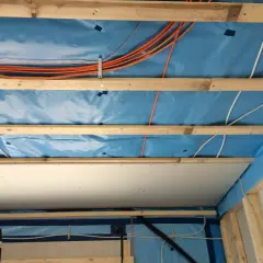 Holzbalken und blaue Dampfsperre für die Befestigung von schweren Lasten an Rigipsdecke. Kabel und Leitungen sind verlegt.