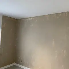 Ein Raum mit ungleichmäßig aufgetragener Farbe auf Kalkzementputz. Die Wände sind in einem hellen Braunton gestrichen, mit sichtbaren Spuren von weißer Farbe.