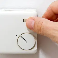 Hand dreht am Regler einer alten Nachtspeicherheizung zur Bedienung.
