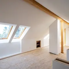 Dachgeschoss im Rohbau, bereit für die Rigipsplattenmontage. Sichtbare Holzbalken und Dachfenster.