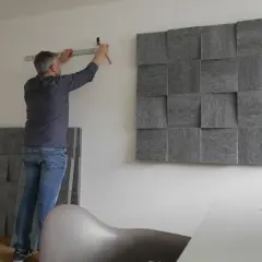 Mann montiert schallabsorbierende Paneele an der Wand, um das Zimmer schalldicht zu machen. Ein Hammer und eine Wasserwaage liegen bereit.