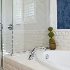 Elegantes Badezimmer mit Duschkabine, Wanne und blau gemusterter Tapete. Die weißen Fliesen und die Tapete ergeben ein stilvolles Ambiente.