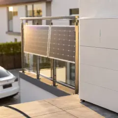 Ein Balkonkraftwerk lädt ein E-Auto. Solarmodule auf dem Balkongeländer und ein Speichergerät mit Ladekabel sind zu sehen.