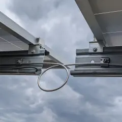 Detailaufnahme von Solarmodulen auf Montageschienen. Ein Kabel ist für die Erdung der PV-Schienen mit einer Schlaufe befestigt.