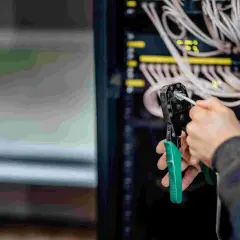 Person crimpt MC4 Stecker für Solarkabel. Im Hintergrund Server-Rack mit vielen Kabeln.