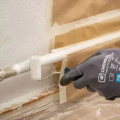 Mit einem kleinen Roller werden Heizungsrohre weiß gestrichen. Die Wand ist abgeklebt, um sie vor Farbspritzern zu schützen.