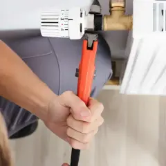 Hand mit Rohrzange dreht am Heizkörperthermostat, um ihn abzuschrauben.