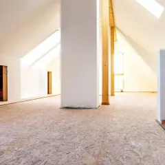 Blick in einen ausgebauten Dachboden mit OSB-Platten als Bodenbelag. Weiße Wände und Dachschrägen mit Fenstern.