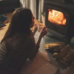 Gemütliches Beisammensein am Kaminfeuer. Eine Frau genießt eine Tasse Tee, während sie die Wärme des Feuers spürt. Heizen ohne Strom ist eine romantische Alternative.