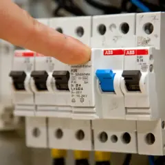Finger betätigt eine elektrische Sicherung, einen FI-Schutzschalter, in einem Sicherungskasten.