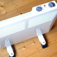 Ein weißer Konvektor mit Rädern steht auf einem Holzboden. Er ist ein Heizgerät, das die Luft erwärmt.