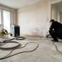 Mann prüft Feuchtigkeit nach Wasserschaden. Bautrockner und Ventilator im Einsatz zur Schimmelprävention.