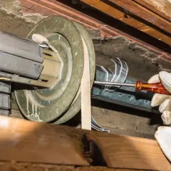 Hand mit Handschuh schraubt am Rollladen. Der alte Rolladengurt wird gewechselt, um den Rollladen wieder funktionsfähig zu machen.