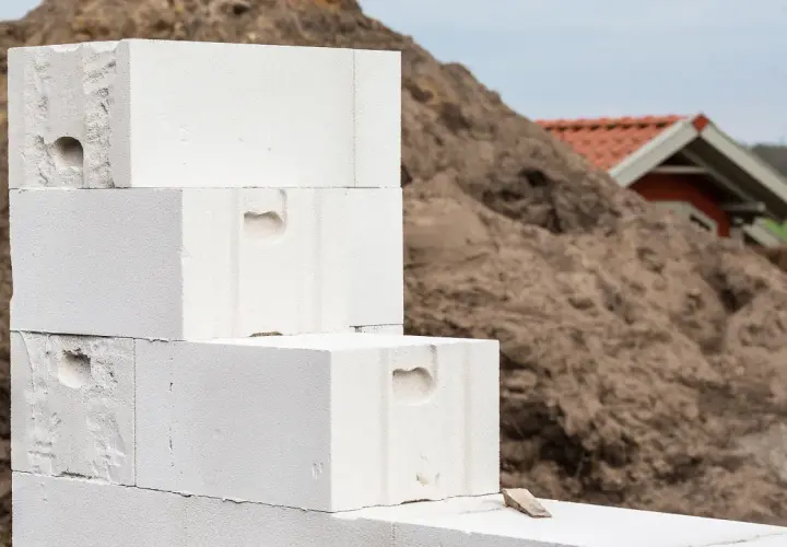 Baustelle: Stapel von Porenbetonsteinen warten darauf, verputzt zu werden. Im Hintergrund ein kleineres Gebäude.