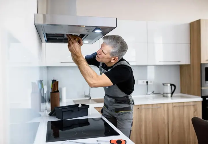 Ein Handwerker repariert eine Dunstabzugshaube, die nicht mehr angeht. Er schaut konzentriert hinein und arbeitet mit Werkzeug.