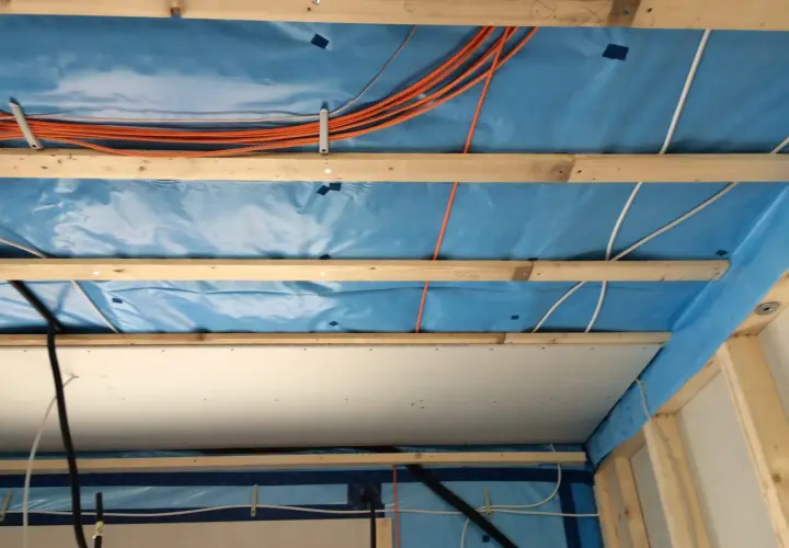 Holzbalken und blaue Dampfsperre für die Befestigung von schweren Lasten an Rigipsdecke. Kabel und Leitungen sind verlegt.