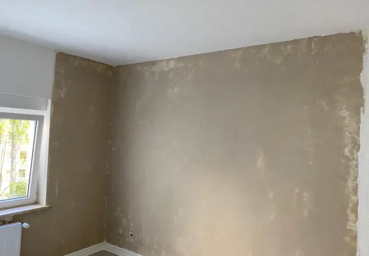 Ein Raum mit ungleichmäßig aufgetragener Farbe auf Kalkzementputz. Die Wände sind in einem hellen Braunton gestrichen, mit sichtbaren Spuren von weißer Farbe.