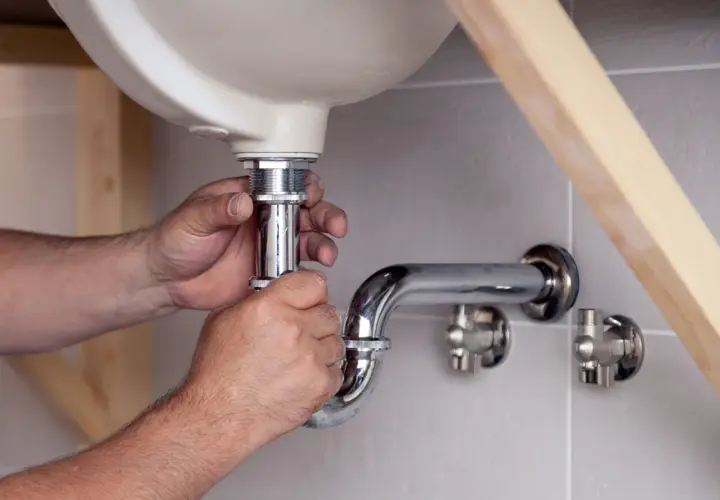Hände montieren ein neues Siphon unter dem Waschbecken. Der alte Siphon muss ausgetauscht werden, um Lecks zu vermeiden.