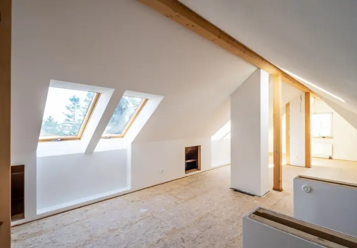 Dachgeschoss im Rohbau, bereit für die Rigipsplattenmontage. Sichtbare Holzbalken und Dachfenster.