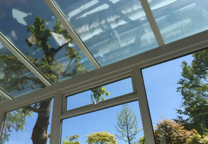 Blick durch ein Fenster in einen Wintergarten mit Glasdach. Bäume spiegeln sich im Glas. Dichtungsarbeiten am Wintergarten sind wichtig.