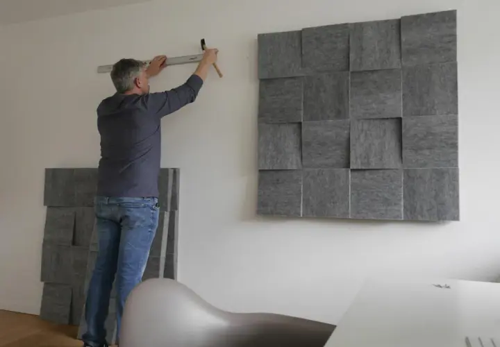 Mann montiert schallabsorbierende Paneele an der Wand, um das Zimmer schalldicht zu machen. Ein Hammer und eine Wasserwaage liegen bereit.