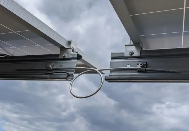 Detailaufnahme von Solarmodulen auf Montageschienen. Ein Kabel ist für die Erdung der PV-Schienen mit einer Schlaufe befestigt.