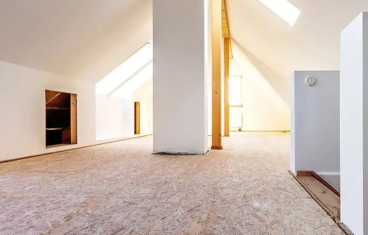 Blick in einen ausgebauten Dachboden mit OSB-Platten als Bodenbelag. Weiße Wände und Dachschrägen mit Fenstern.