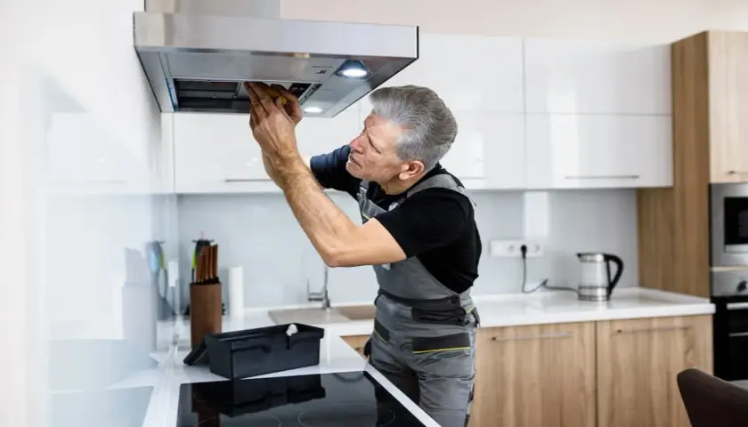 Ein Handwerker repariert eine Dunstabzugshaube, die nicht mehr angeht. Er schaut konzentriert hinein und arbeitet mit Werkzeug.