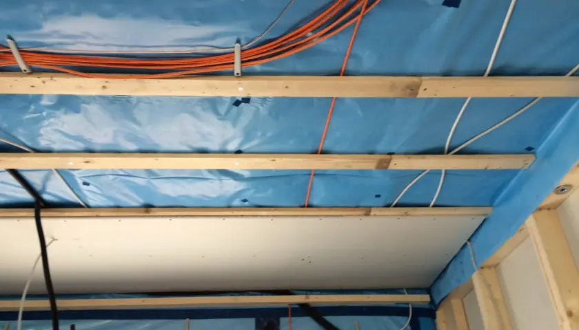 Holzbalken und blaue Dampfsperre für die Befestigung von schweren Lasten an Rigipsdecke. Kabel und Leitungen sind verlegt.