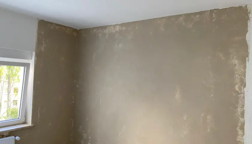 Ein Raum mit ungleichmäßig aufgetragener Farbe auf Kalkzementputz. Die Wände sind in einem hellen Braunton gestrichen, mit sichtbaren Spuren von weißer Farbe.
