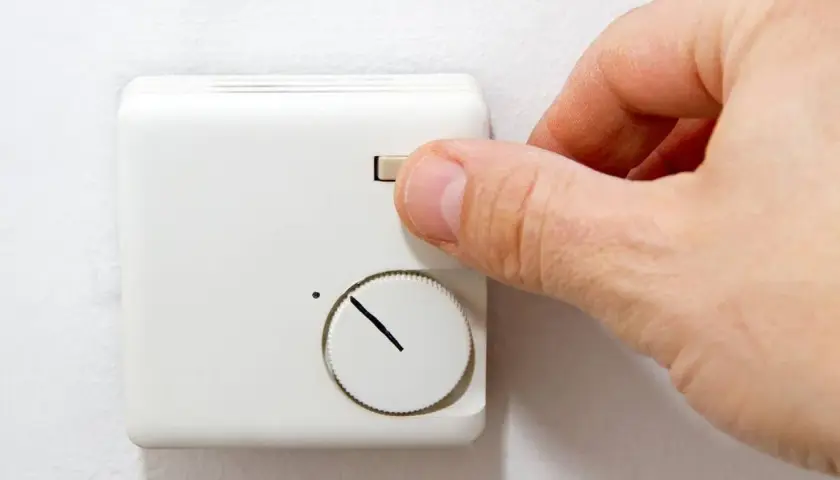 Hand dreht am Regler einer alten Nachtspeicherheizung zur Bedienung.