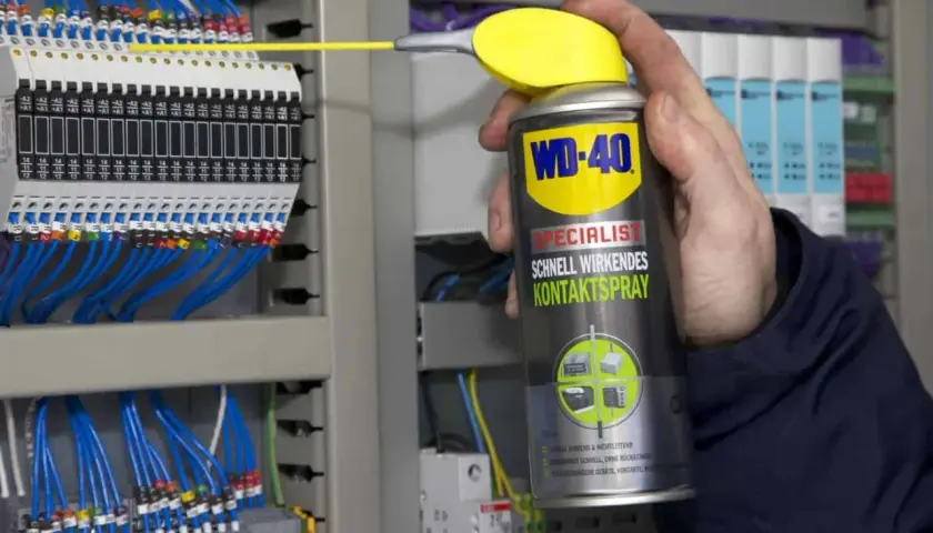 Hand sprüht mit WD-40 Kontaktspray auf elektrische Klemmen, um korrodierte Kontakte zu reinigen und die Funktion sicherzustellen.