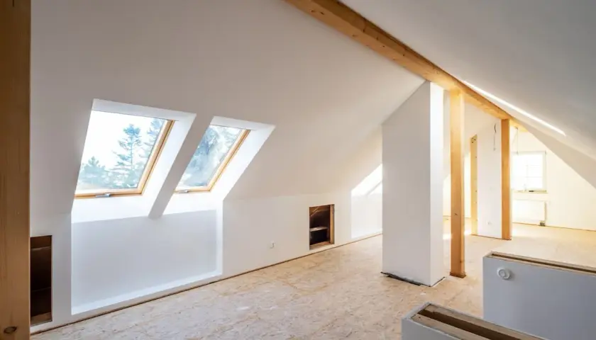 Dachgeschoss im Rohbau, bereit für die Rigipsplattenmontage. Sichtbare Holzbalken und Dachfenster.