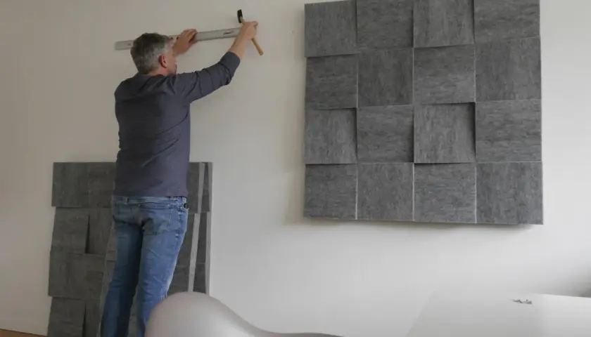 Mann montiert schallabsorbierende Paneele an der Wand, um das Zimmer schalldicht zu machen. Ein Hammer und eine Wasserwaage liegen bereit.