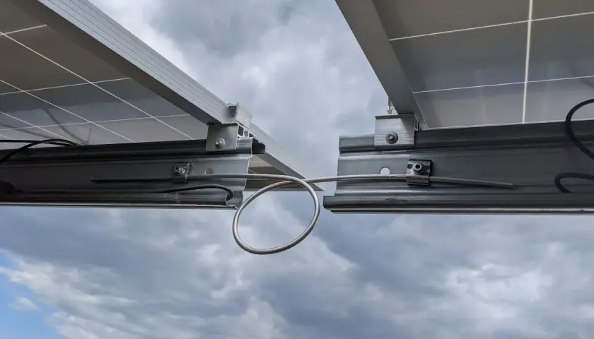 Detailaufnahme von Solarmodulen auf Montageschienen. Ein Kabel ist für die Erdung der PV-Schienen mit einer Schlaufe befestigt.