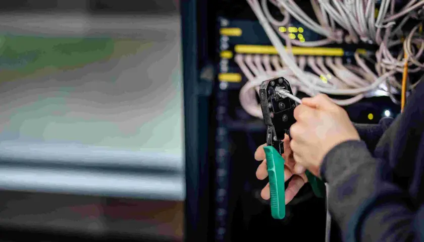 Person crimpt MC4 Stecker für Solarkabel. Im Hintergrund Server-Rack mit vielen Kabeln.