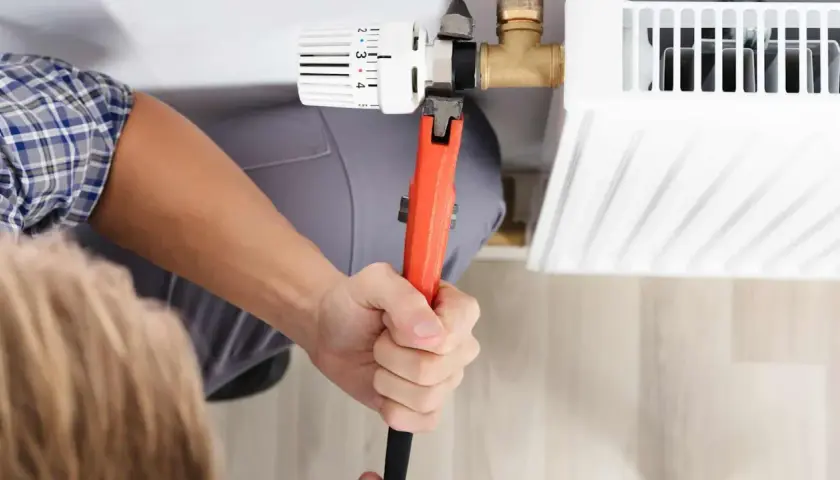 Hand mit Rohrzange dreht am Heizkörperthermostat, um ihn abzuschrauben.