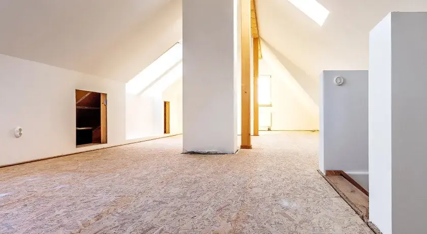 Blick in einen ausgebauten Dachboden mit OSB-Platten als Bodenbelag. Weiße Wände und Dachschrägen mit Fenstern.