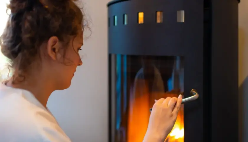 Frau öffnet Kamin. Die Drosselklappe des Ofenrohrs ist offen, um das Feuer zu speisen.