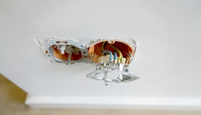Einbau einer Doppelsteckdose: Freiliegende Kabel und orangefarbene Unterputzdose in einer Decke.