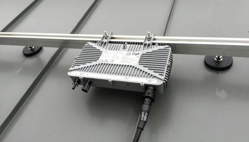 Ein Mikrowechselrichter wird auf einer Schiene montiert, die auf einem Metalldach befestigt ist. Die Montage ist einfach und sicher.