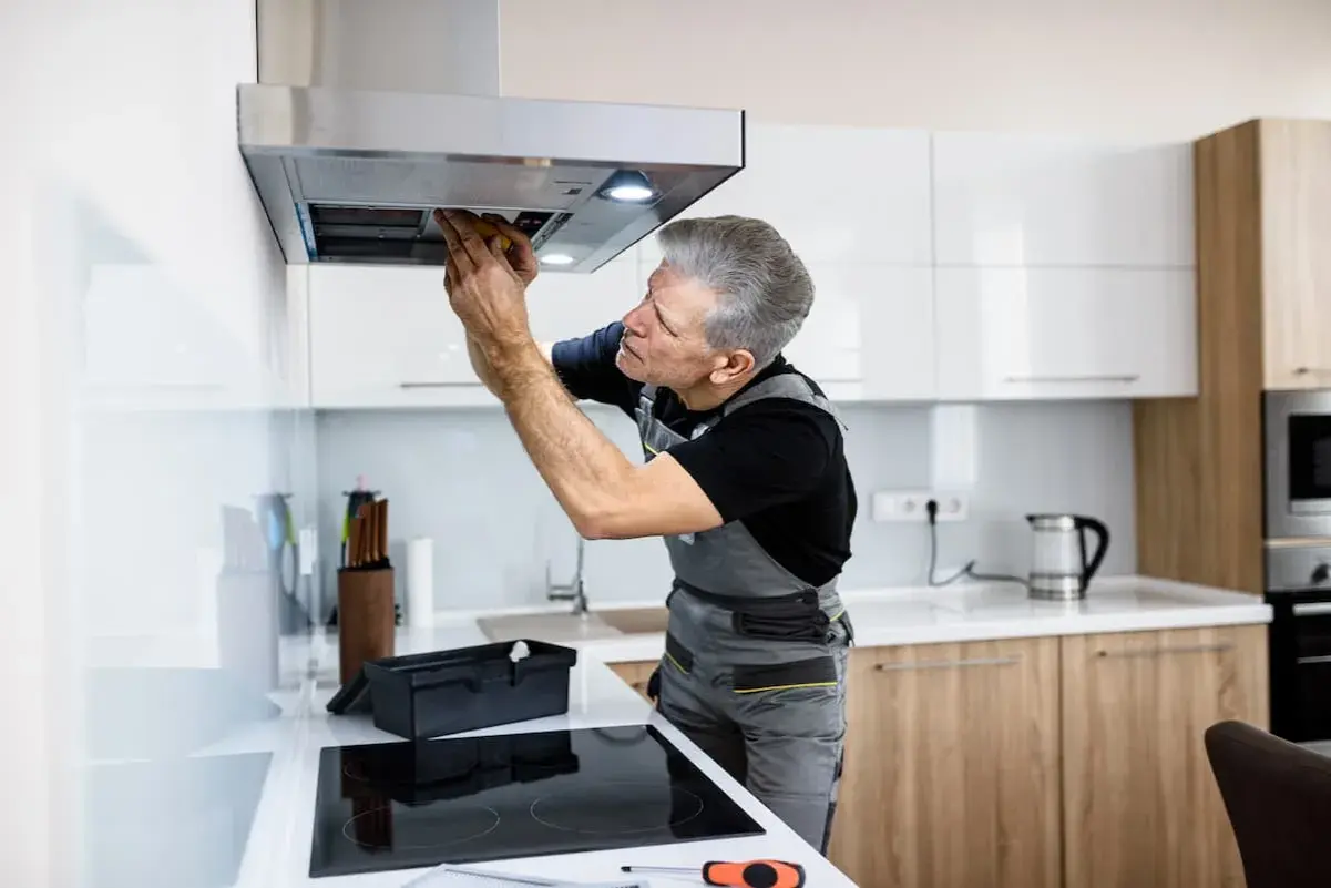 Ein Handwerker repariert eine Dunstabzugshaube, die nicht mehr angeht. Er schaut konzentriert hinein und arbeitet mit Werkzeug.
