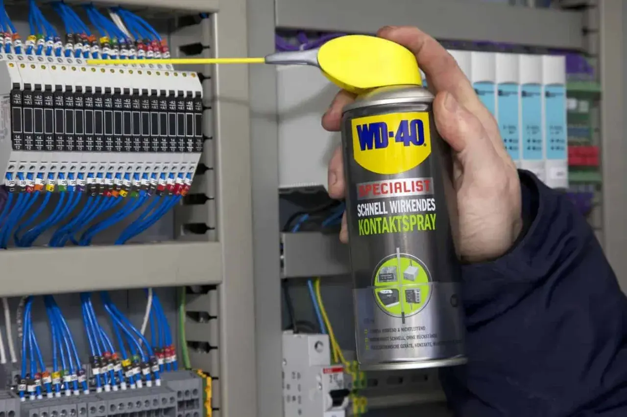 Hand sprüht mit WD-40 Kontaktspray auf elektrische Klemmen, um korrodierte Kontakte zu reinigen und die Funktion sicherzustellen.