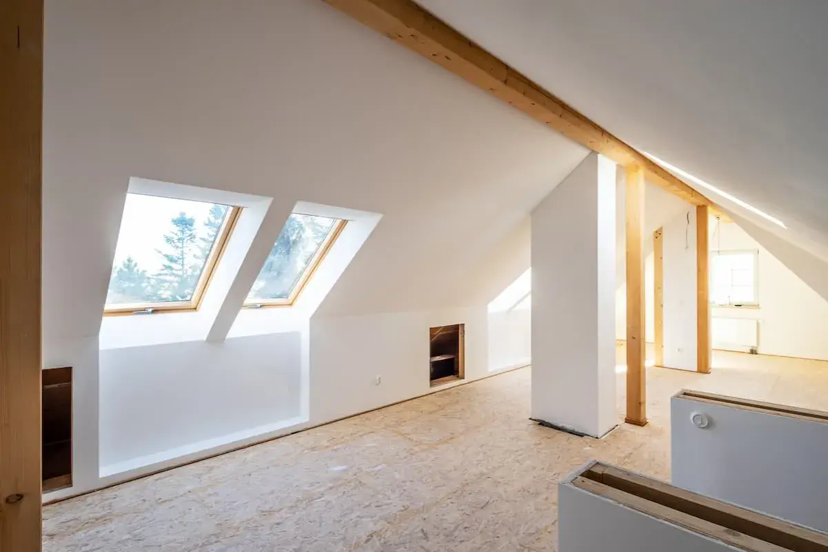 Dachgeschoss im Rohbau, bereit für die Rigipsplattenmontage. Sichtbare Holzbalken und Dachfenster.