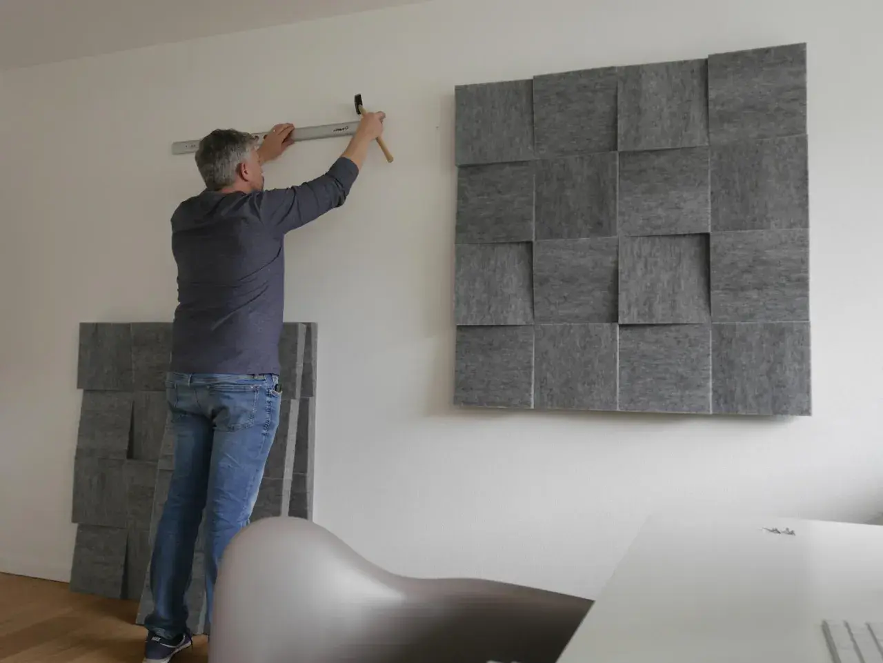 Mann montiert schallabsorbierende Paneele an der Wand, um das Zimmer schalldicht zu machen. Ein Hammer und eine Wasserwaage liegen bereit.